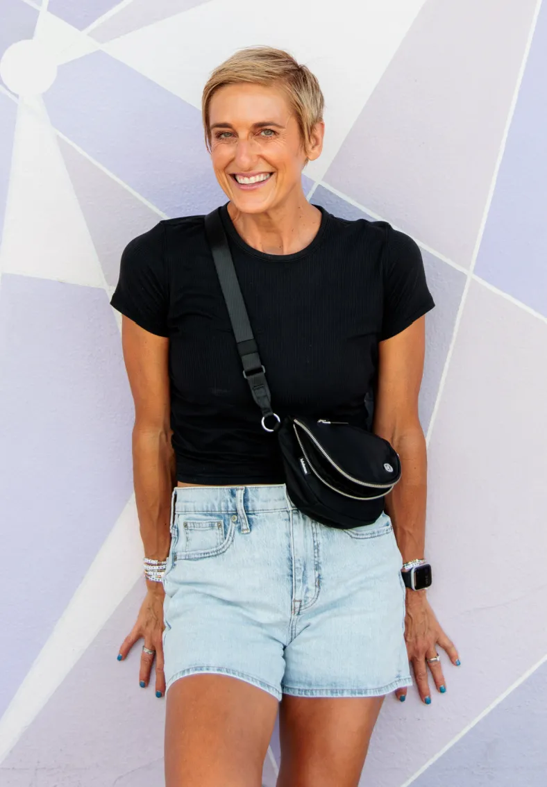Julie Voris standing against a colorful wall with blue jean shorts on