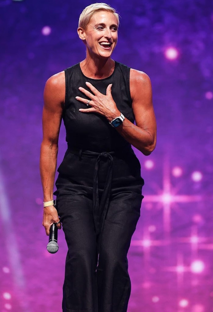 Julie Voris in black jumpsuit speaking on stage
